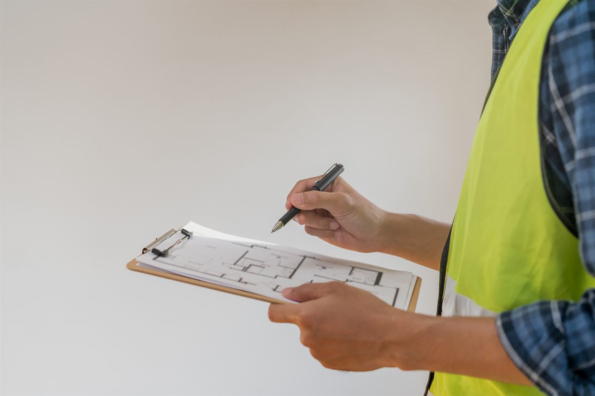 Building inspector in hi-vis vest reviewing floor plans on a clipboard